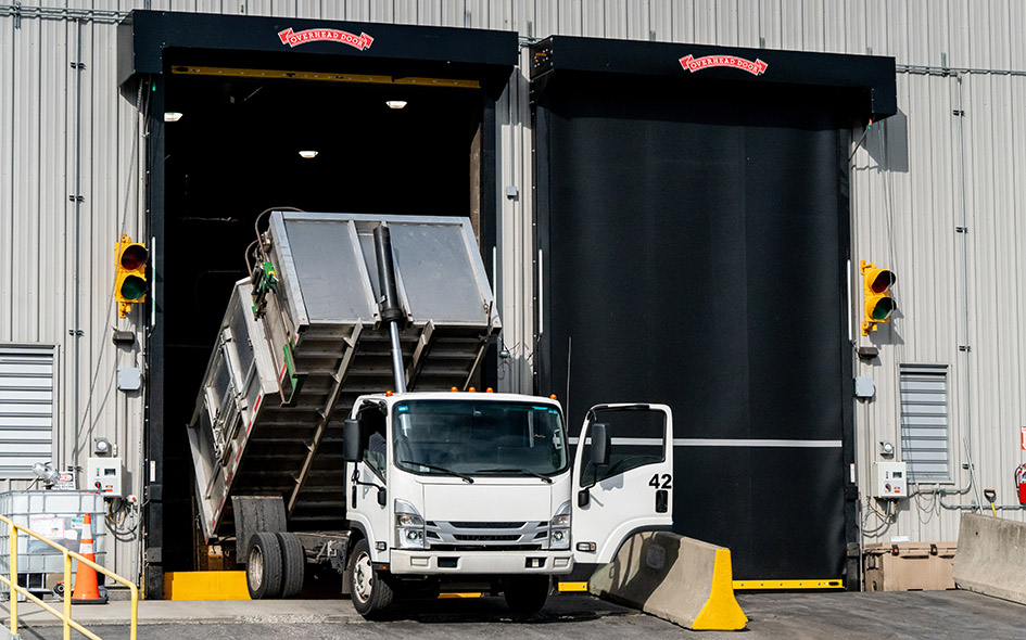 white truck dumping it's body into a space in a commercial building with a black commercial doors